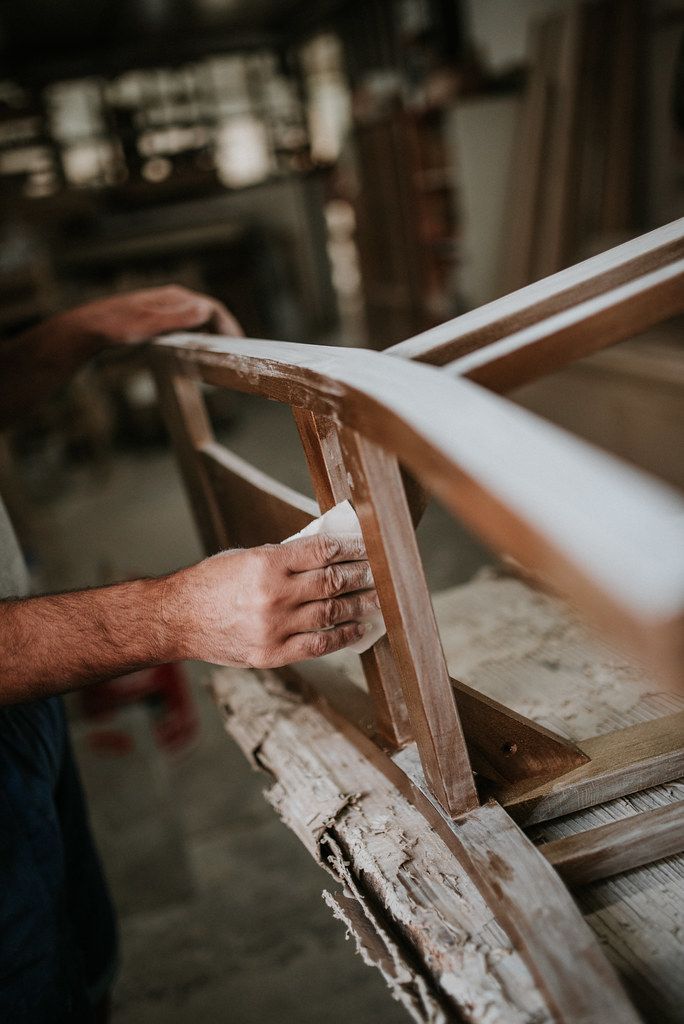 Carpenter sanding a wooden chair frame in a workshop